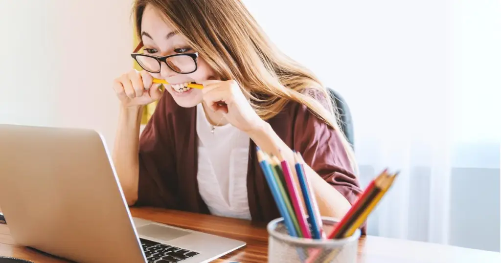 woman biting on pencil while working on pc